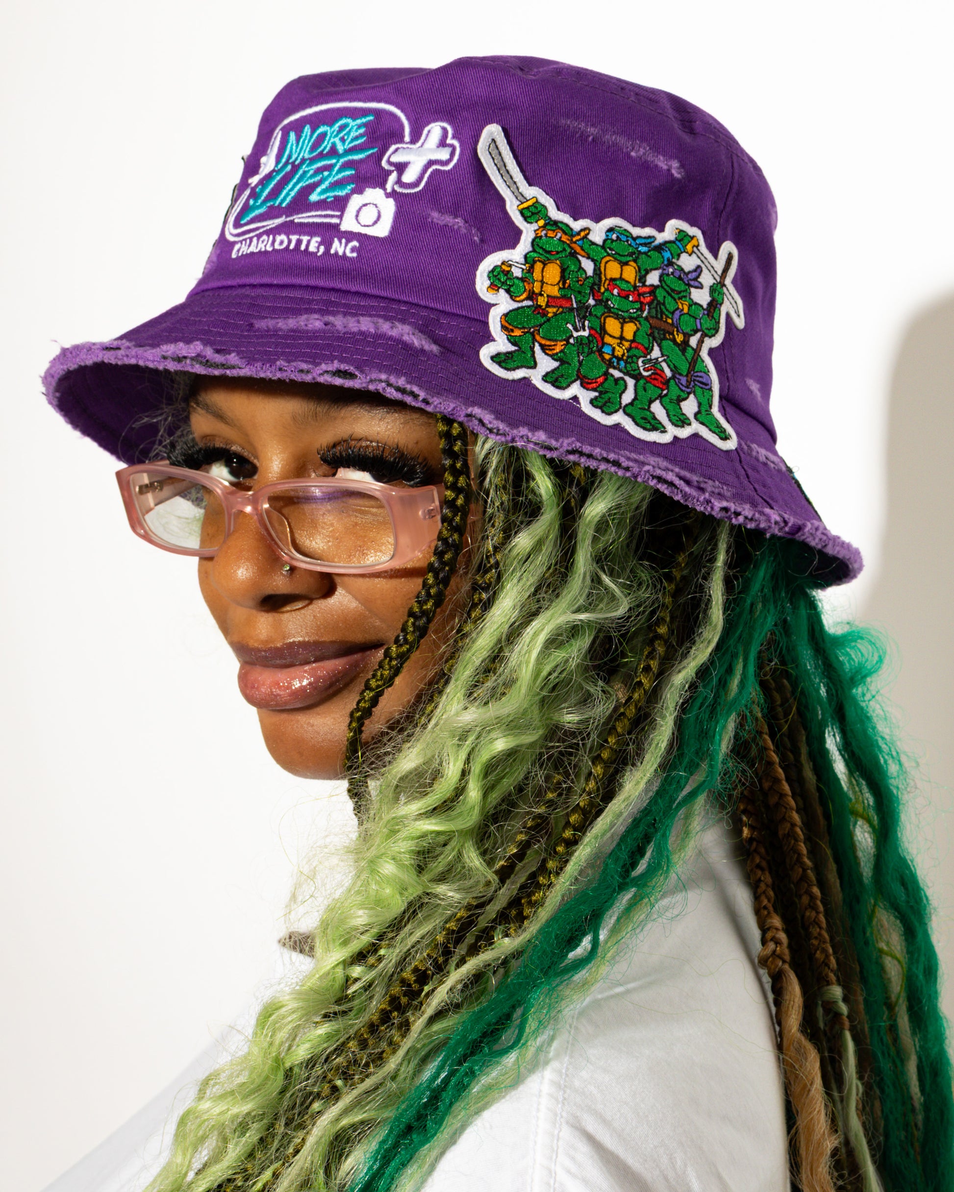 More Life CLT Custom Deluxe Bucket Hat Green – back view showing More Life Charlotte NC logo patch and daisy flowers on olive green distressed base
