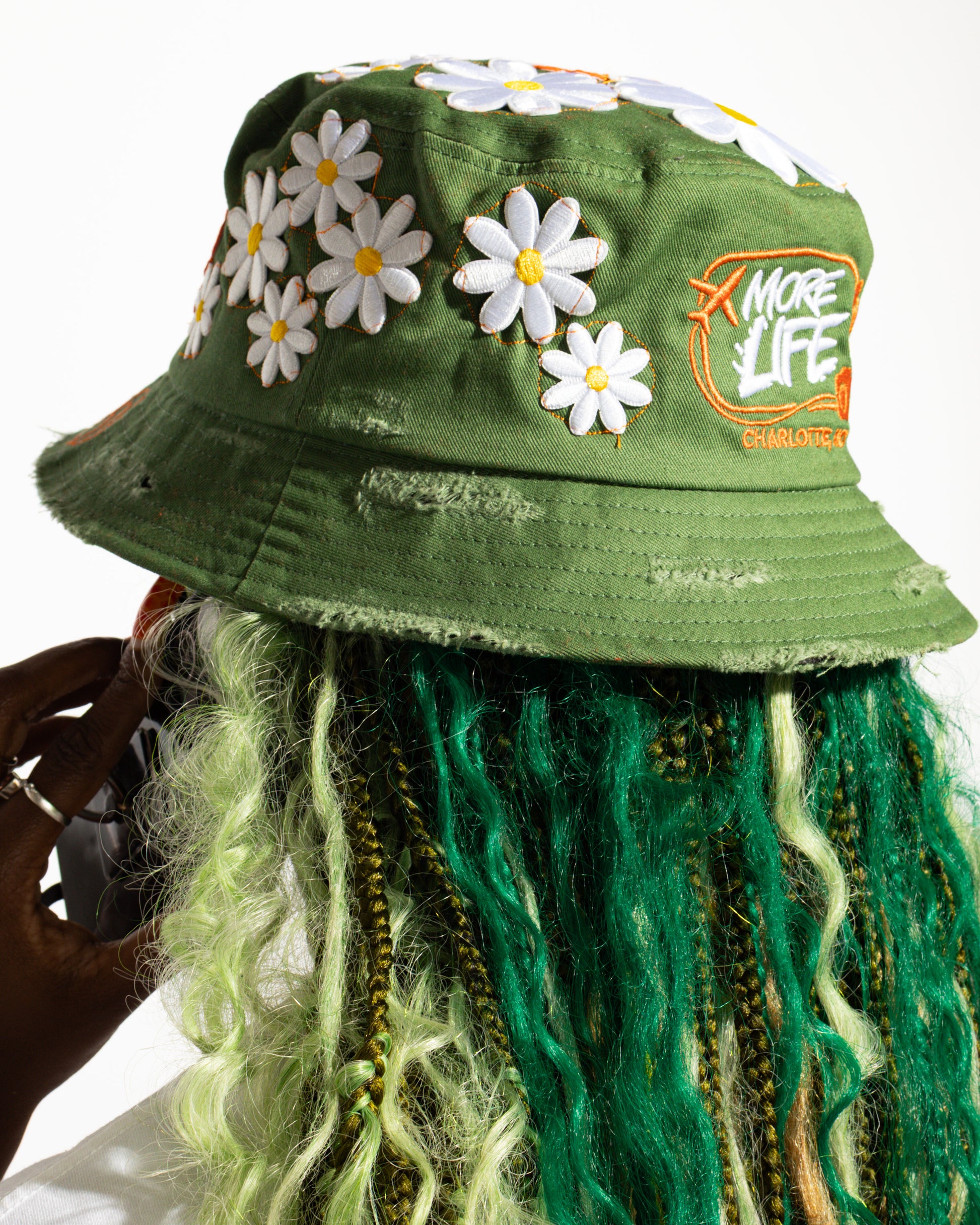 More Life CLT Custom Deluxe Bucket Hat Green – top view showing full daisy flower patch coverage on olive green distressed base