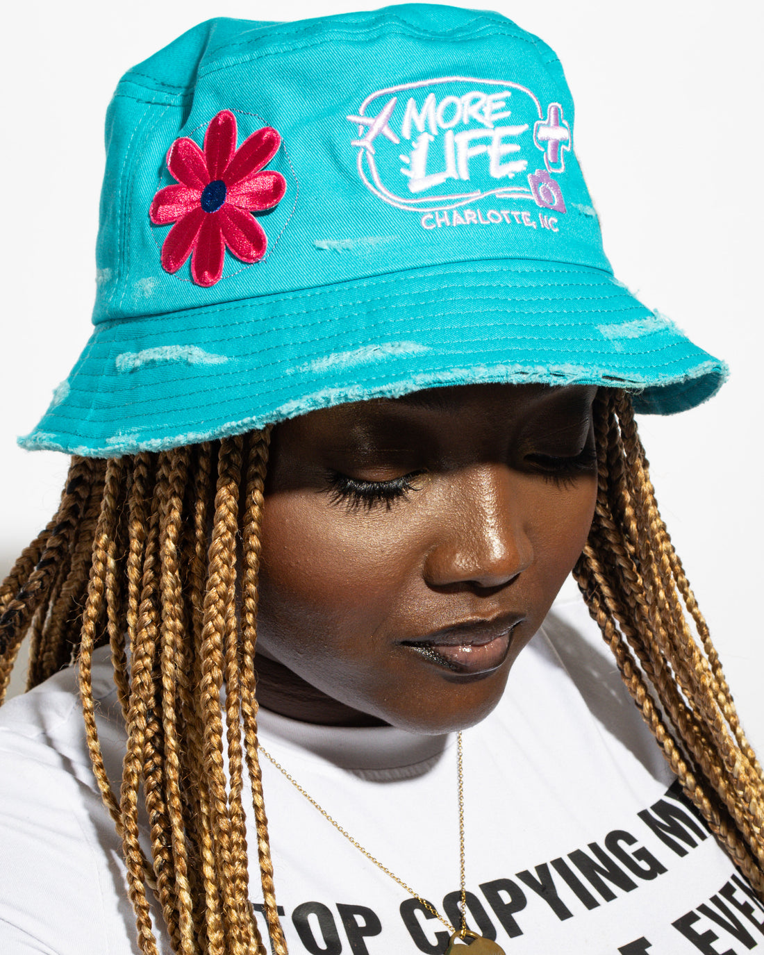 More Life CLT Daisy New York Patchwork Distressed Bucket Hat Teal – front view on model showing pink daisy patch and More Life Charlotte NC logo