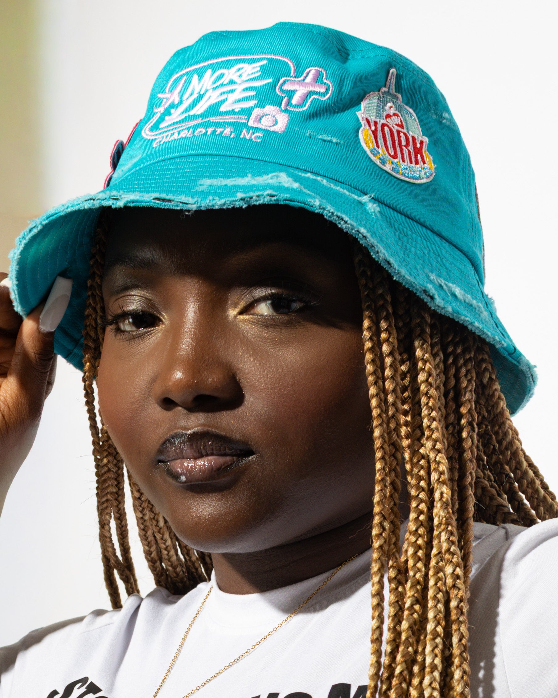 More Life CLT Daisy New York Patchwork Distressed Bucket Hat Teal – side view on model showing More Life Charlotte NC logo and New York city badge patch